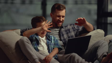 Papá-Hijo-Teniendo-Videollamada-Portátil-En-Casa.-Padre-Hijo-Mirando-La-Pantalla-De-La-Computadora.