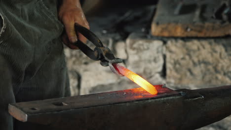 a skilled blacksmith beats with a hammer on a red-hot metal blank