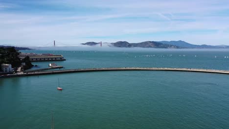 drone flyover of aquatic park pier in san francisco with the golden gate bridge in the background shrouded with light fog on a sunny day