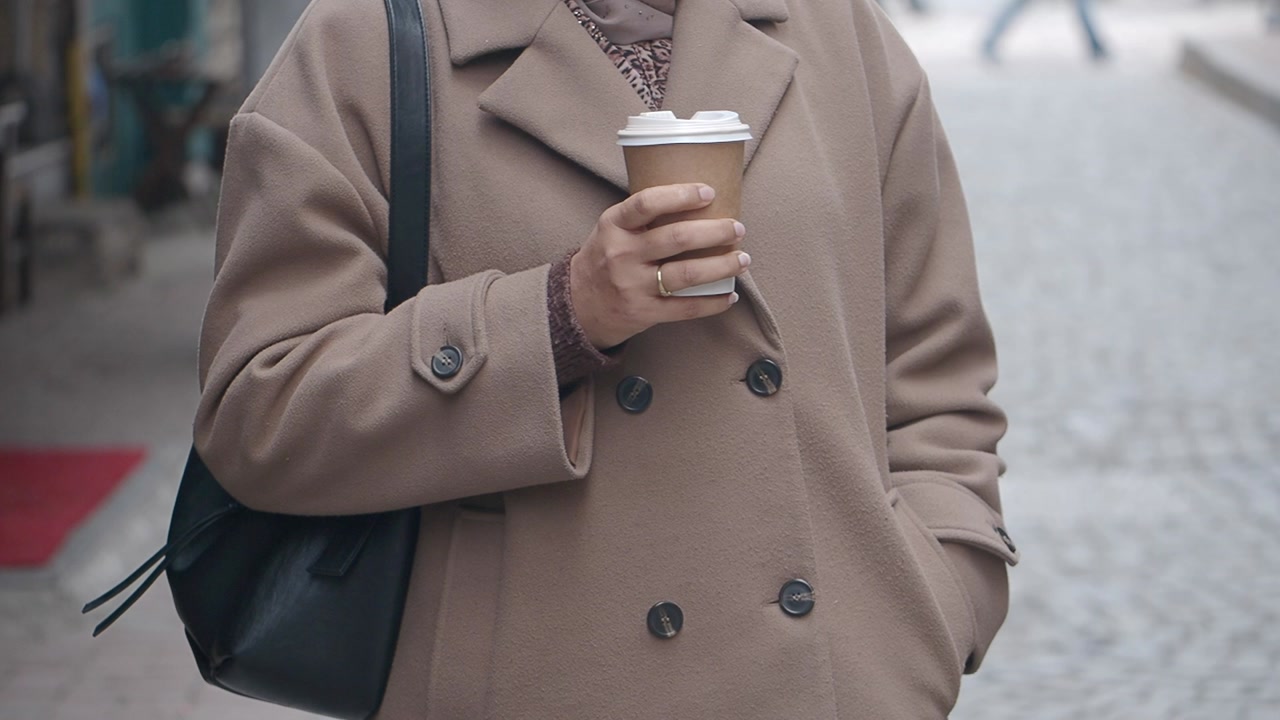 Woman in Beige Coat Holding Takeaway Coffee Cup on Street