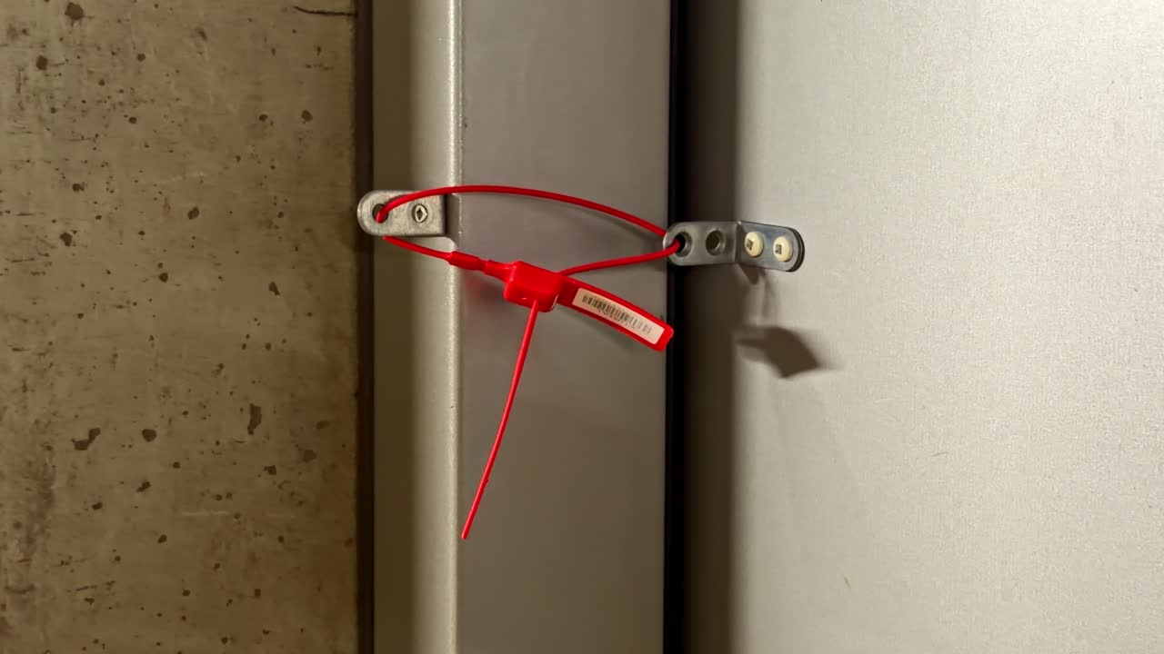 A red cable tie secures a metal latch on an industrial door, highlighting safety measures. Useful for security and manufacturing content