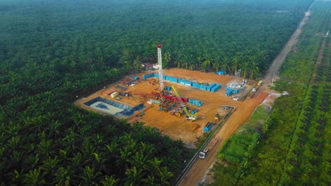 Cinematic-Drone-Shot-of-Onshore-Drilling-and-Workover-Rig-structure-and-Rig-equipment-for-oil-exploration-and-exploitation-in-the-middle-of-jungle-surrounded-by-palm-oil-trees-during-sunset-time