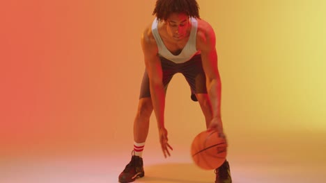 Video-of-biracial-male-basketball-player-bouncing-ball-on-orange-to-yellow-background