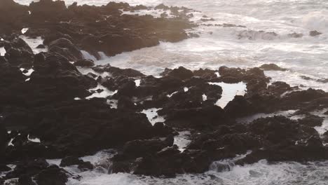 wave crashing into the rocky coastline at flores island, aerial