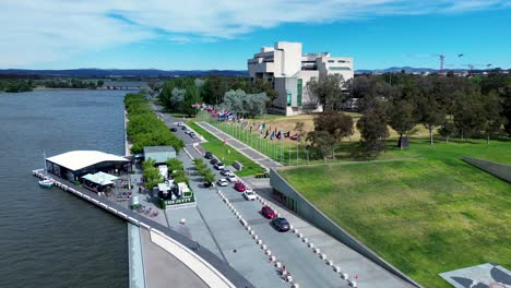 Drone-aerial-shot-National-art-gallery-The-Jetty-international-flags-boardwalk-foreshore-park-Lake-Burley-Griffin-Parliamentary-zone-Canberra-travel-tourism-ACT-Australia-4K