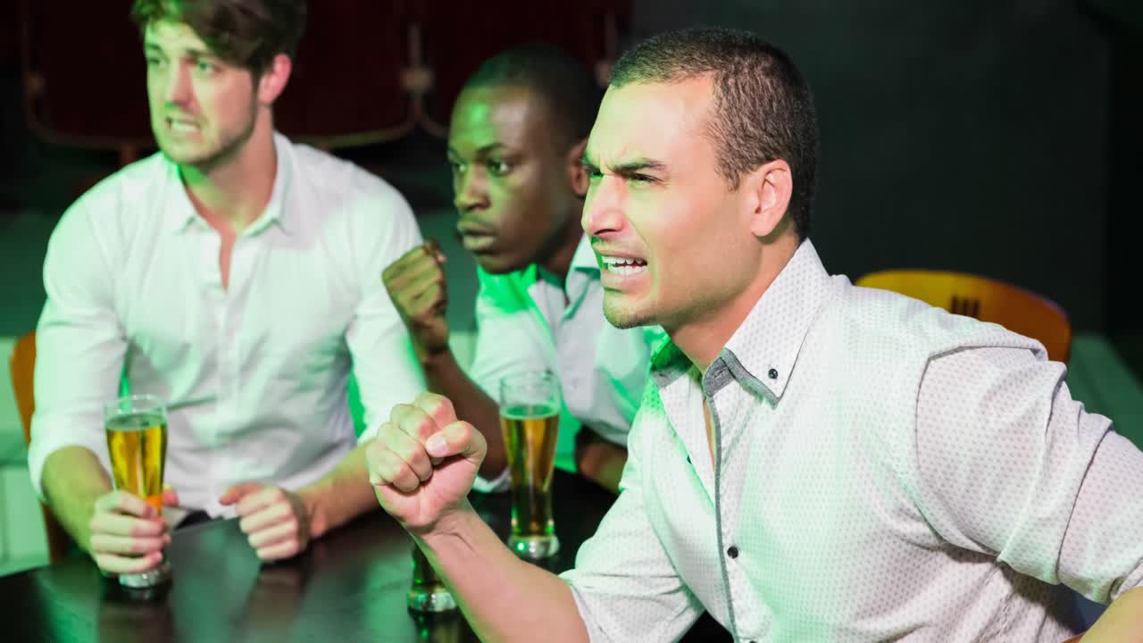 tensa diversidad de aficionados al deporte concentrados en ver el juego en el bar, levantando los puños y bebiendo