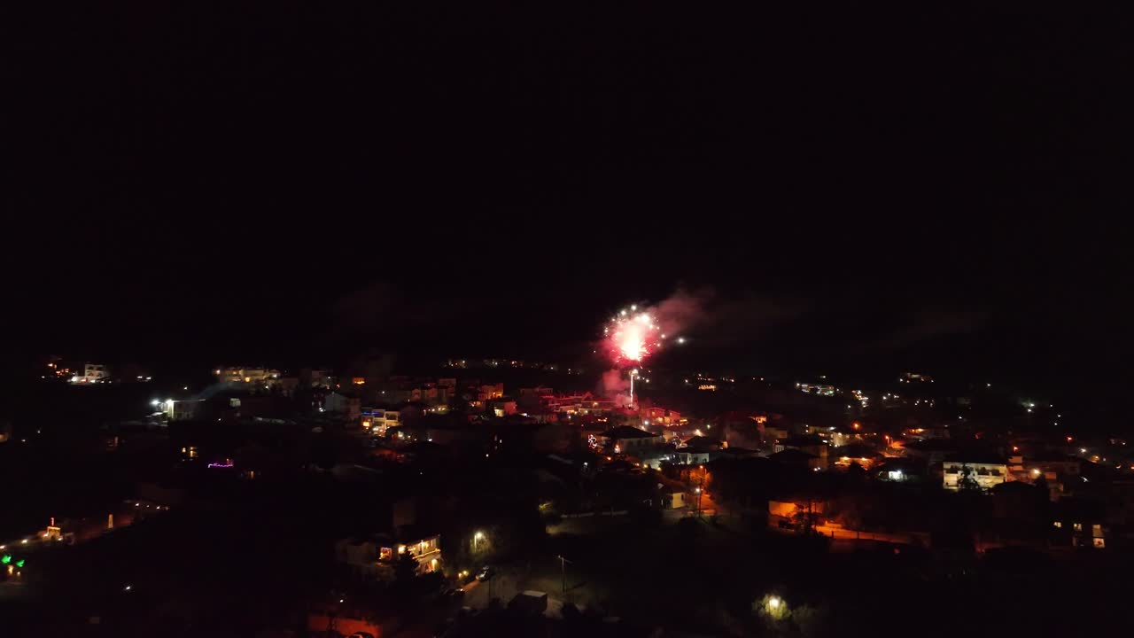 Flying above the dim lit town, towards the colorful sparkling fireworks on New Year's Eve. Aerial close up