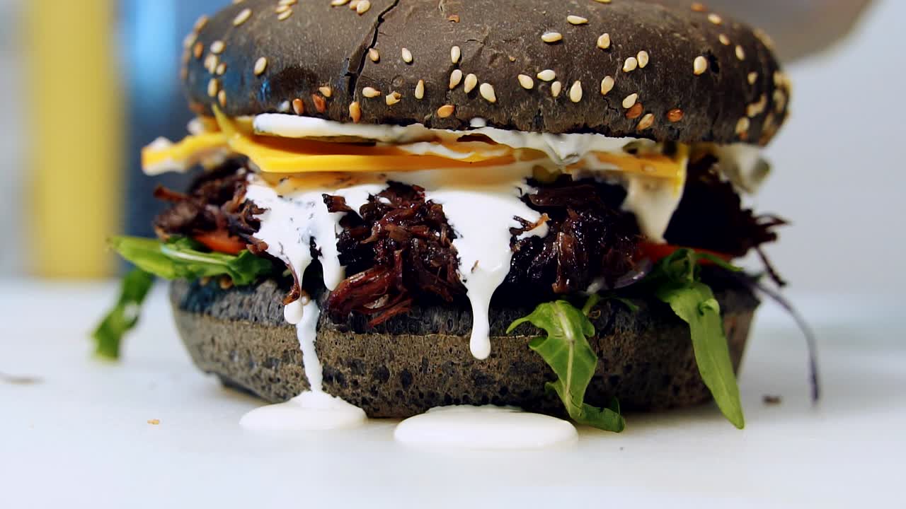Juicy burger preparation. Chef is cooking healthy hamburger of black bun with vegetables and white tasty sauce. Close-up