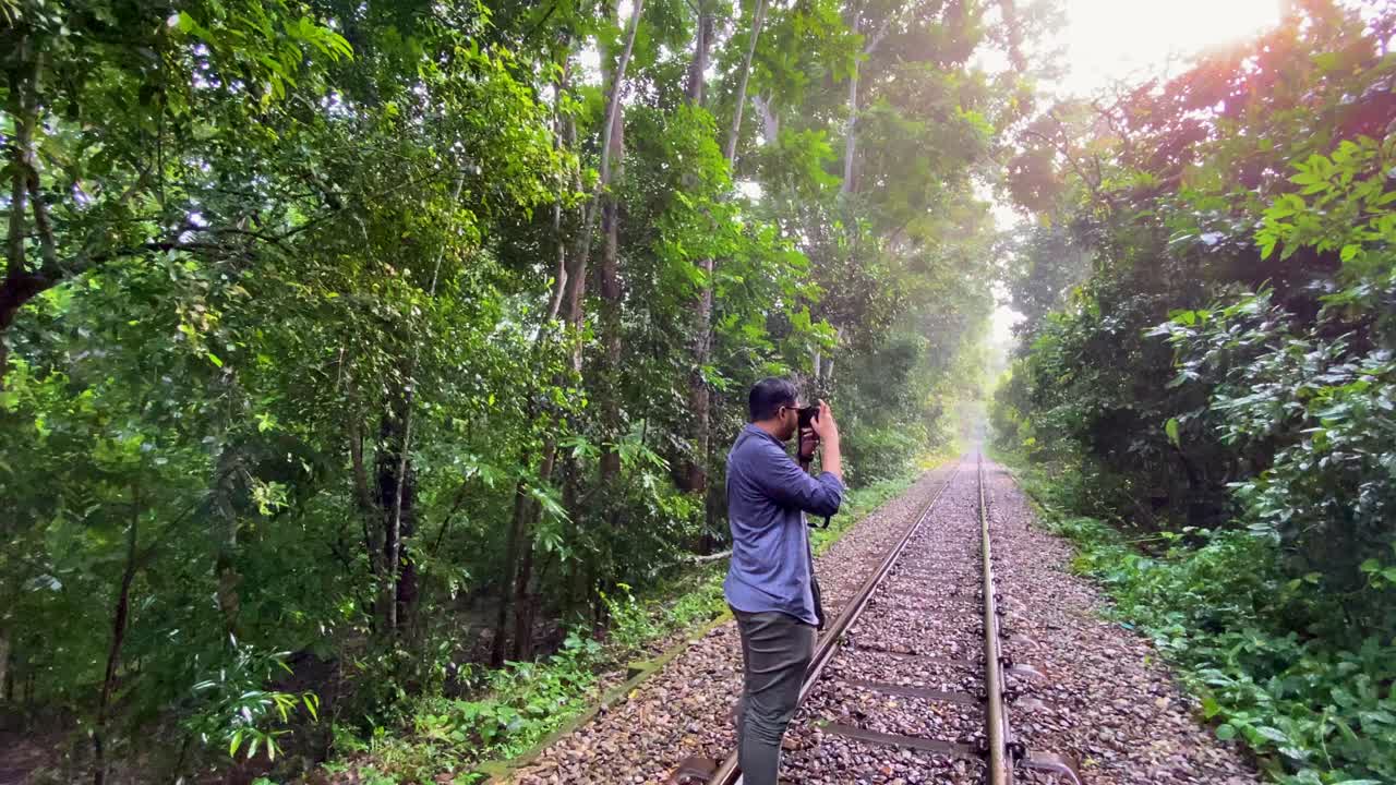 A photographer on the rail tracks in the forest of Lawachara National Park, nature photography in the green, tropical forest in Bangladesh, sun shining through green trees