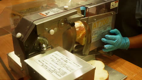un panadero cortando una rebanada de pan de levadura usando una máquina dentro de una panadería local en bangkok, tailandia