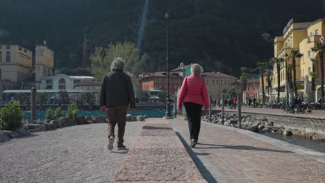 Pareja-De-Ancianos-Camina-Y-Se-Abraza-En-El-Muelle-De-Riva-Del-Garda,-Italia