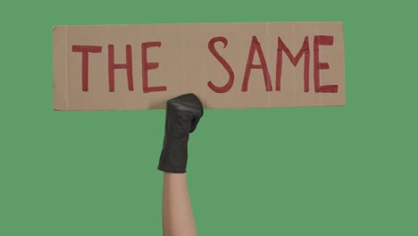 la mano con guantes negros levanta un cartel de cartón lo mismo. concepto de igualdad y unidad. pluralidad de violencia y racismo anti-negro. aislado una pantalla verde, clave de croma. cerca. cámara lenta