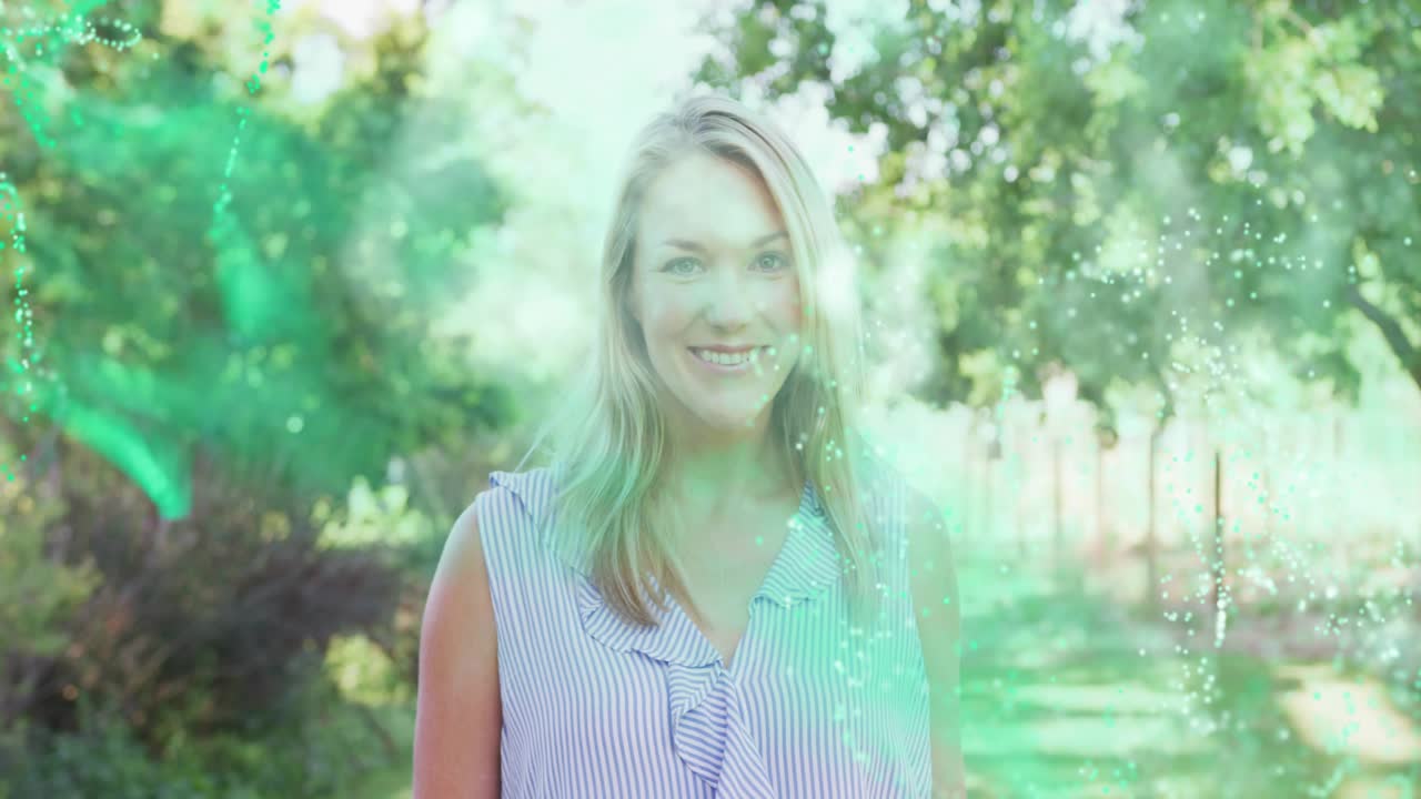 Donna in piedi su un sentiero illuminato dal sole, con particelle tecnologiche che appaiono da sinistra, sfumando e rivelando un sorriso.
