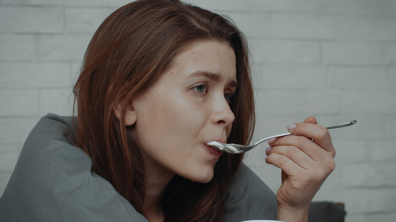Woman eating soup while sick in bed