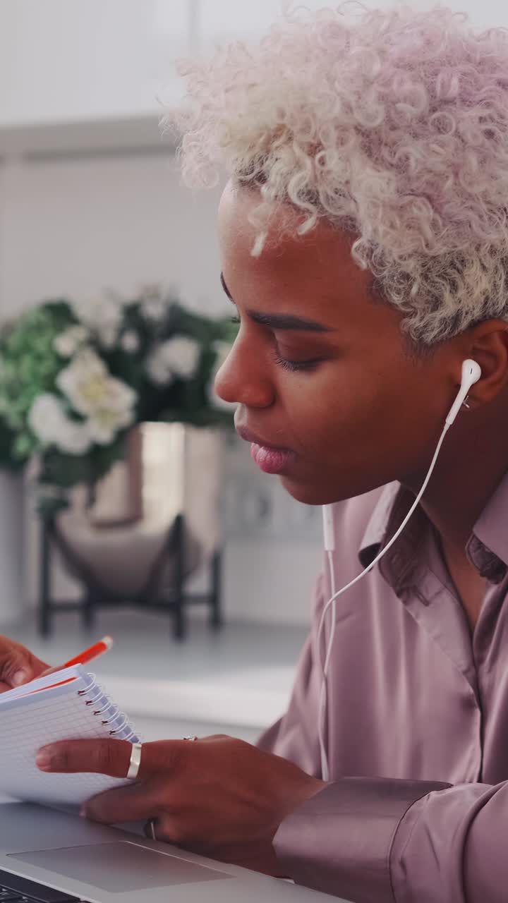 Giovane donna concentrata che prende appunti mentre ascolta musica a casa