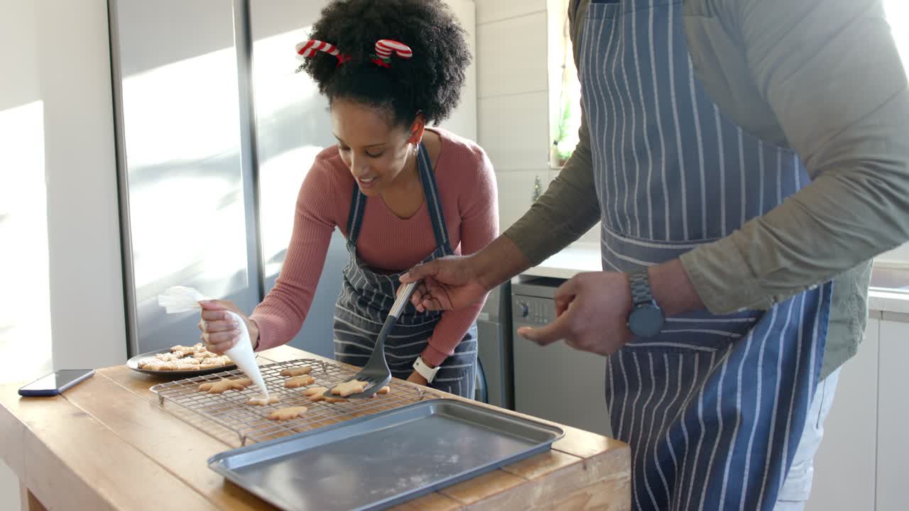 Melihat kue kering, pasangan Afrika-Amerika menghias dengan piping icing, memindahkannya ke atas loyang di kitchen island