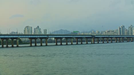 Seoul-City-River-Stadtpark-Mit-Brücke-Am-Abend-Mit-Gebäuden-Und-Wolkenkratzern-Weitwinkelpanorama-Mit-Wasser,-Wellen-Und-Himmel