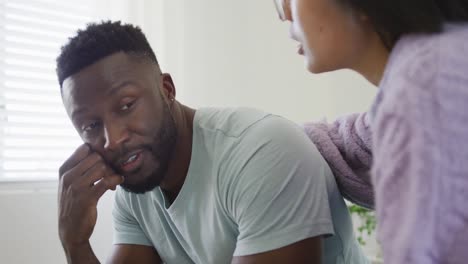 Sad-diverse-couple-sitting-on-couch-and-talking-in-bedroom