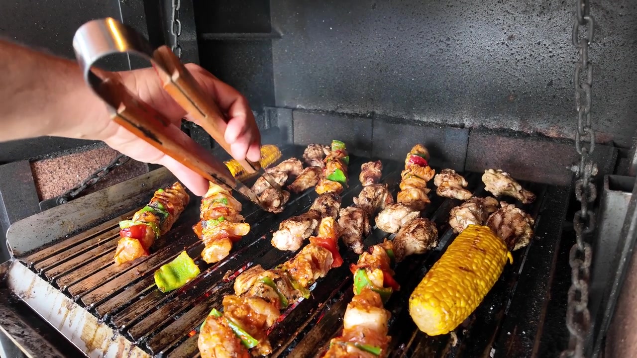 Spiedini di carne e mais alla griglia su un barbecue a carbone.