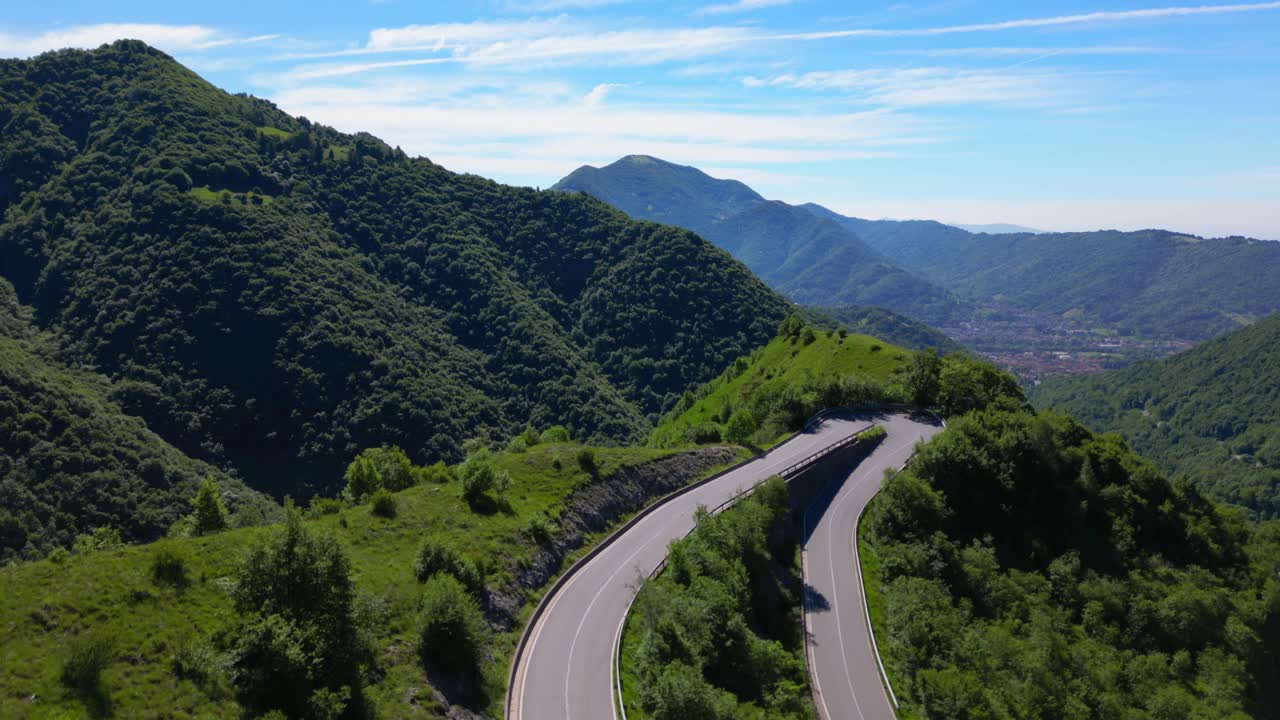 Aerial top-down view of cars navigating a sharp mountain curve surrounded by green vegetation. Shot at Selvino, Italy (Selvino, Italia)