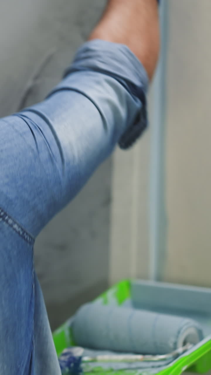 guy in denim shirt and gloves paints room corner with brush backside view. Black worker changes style of new apartment. Restore work
