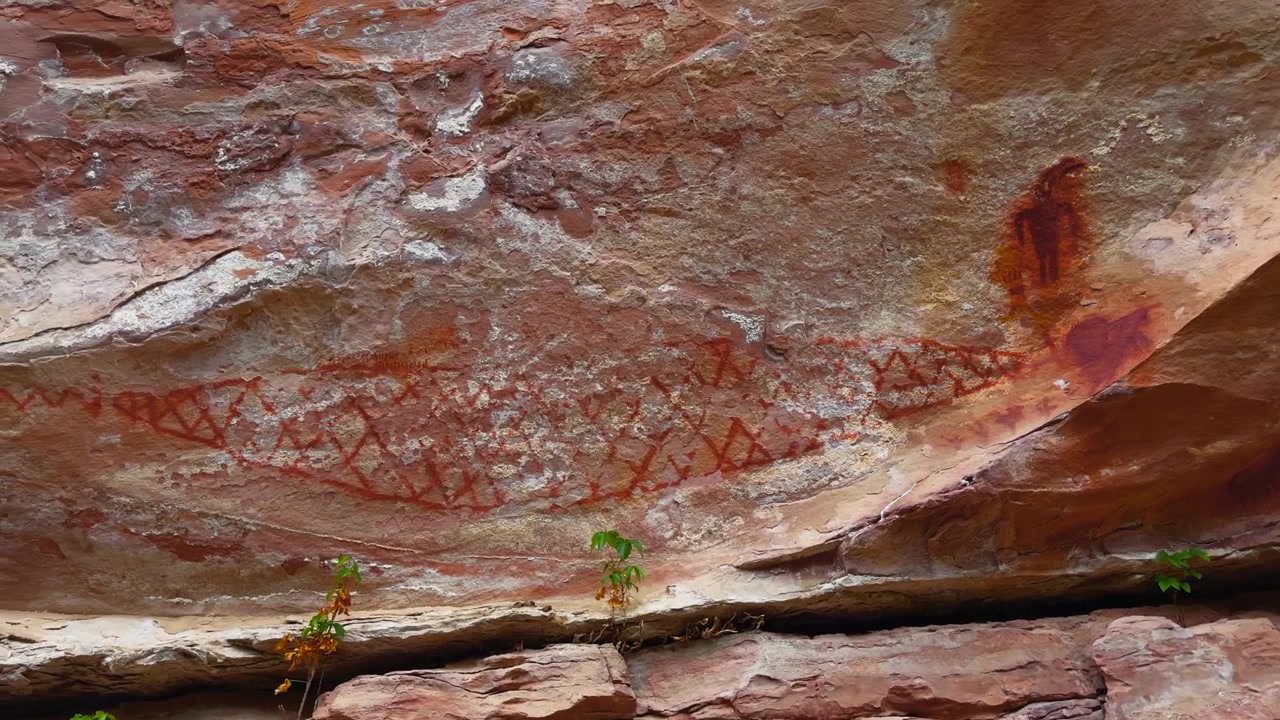 Pittogramma geometrico rosso di figure antropomorfe a forma di pesce o bocca dipinte sul soffitto di un riparo roccioso in arenaria