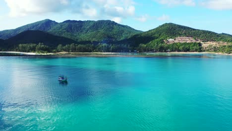 Fishing-boat-leaving-calm-blue-turquoise-lagoon-of-tropical-island,-sailing-toward-open-sea-on-a-bright-morning-with-cloudy-sky-in-Thailand