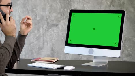 business, deadline and technology concept - man with computer calling on smartphone and pointing to the monitor. green screen mock-up display
