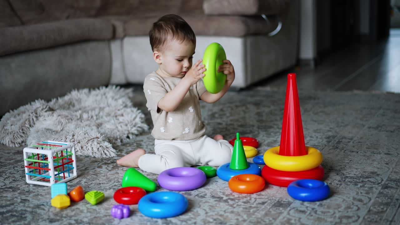 One year old toddler playing with his toys on the floor. Kid takes a ring from pyramid and walks away with it.