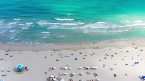 aerial leftward drone glide over south beach, miami, capturing sunbathers, turquoise waters, and gentle rolling surf from a dreamy coastal perspective.