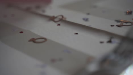 Close-up-of-wedding-confetti-on-a-table-with-a-white-tablecloth,-with-small-hearts-and-glasses-and-rings