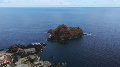 ilhéu mole, rocky islet off coast of porto moniz, with town and natural lava pools in view, madeira, portugal. aerial drone, copy space