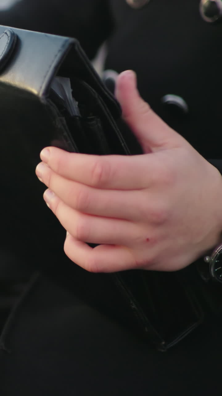 primer plano de un individuo con ropa negra sentado, buscando en un maletín un documento, el fondo presenta un objeto en movimiento poco claro con efecto de luz