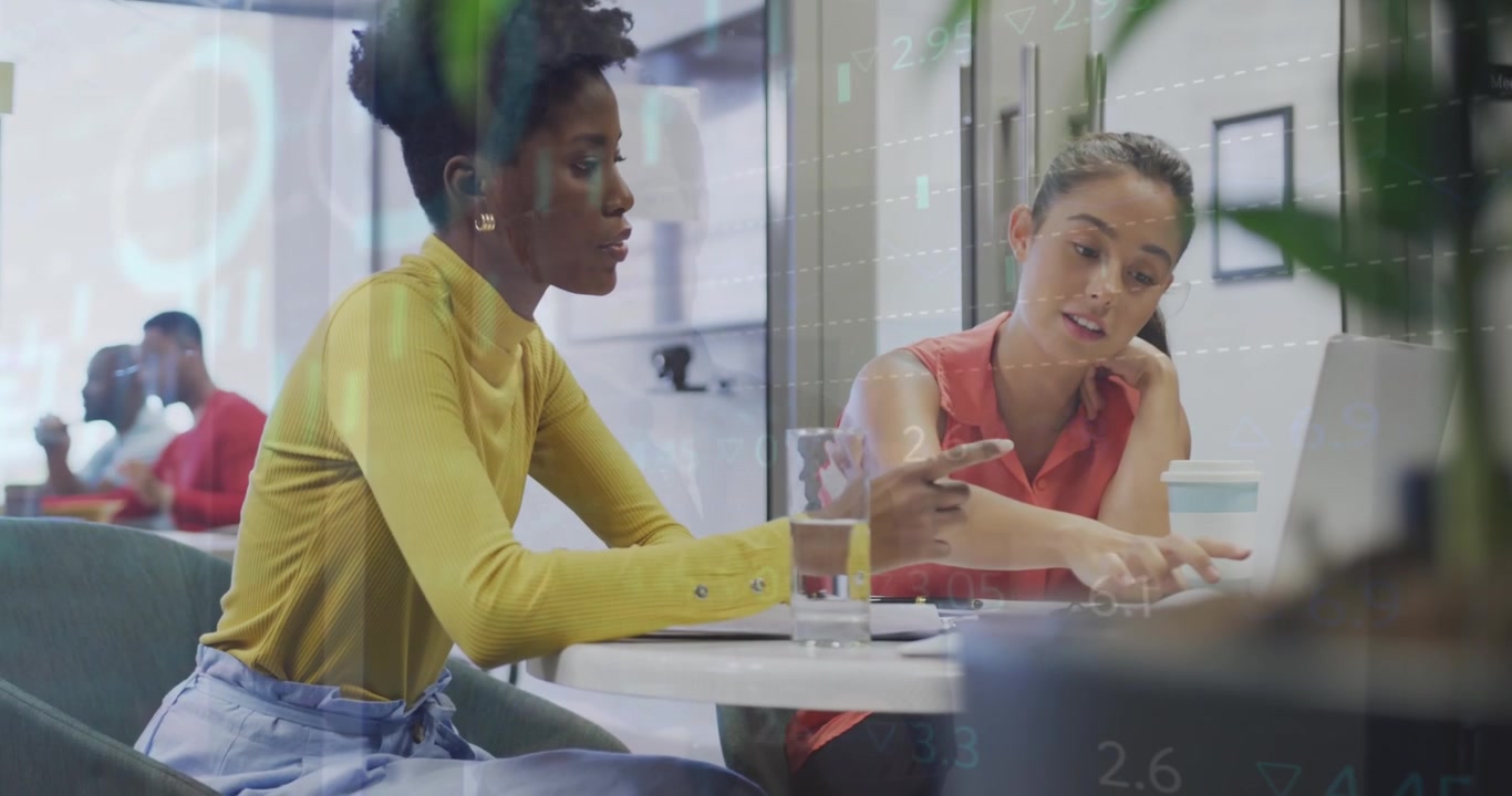Two Diverse Businesswomen Collaborating on Laptop with Financial Data Overlay