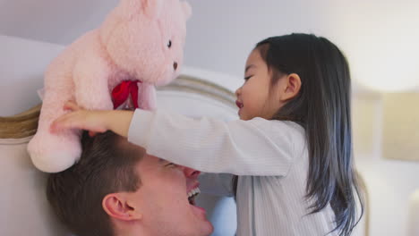 Family-With-Two-Dads-In-Bed-At-Home-Playing-Game-With-Daughter-And-Her-Soft-Toy