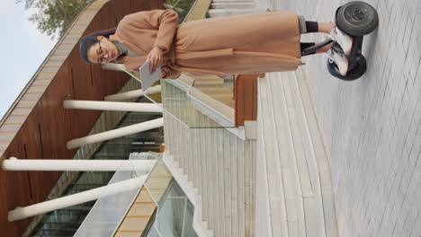 woman riding self-balancing scooter while using tablet in urban setting