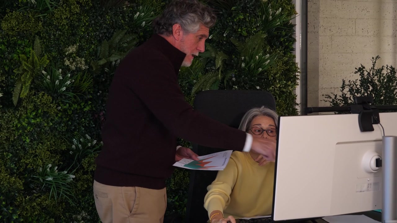 Mature businessman standing near seated female colleague to review computer monitor content. Concept for office mentorship, data analysis, team collaboration, and workflow.