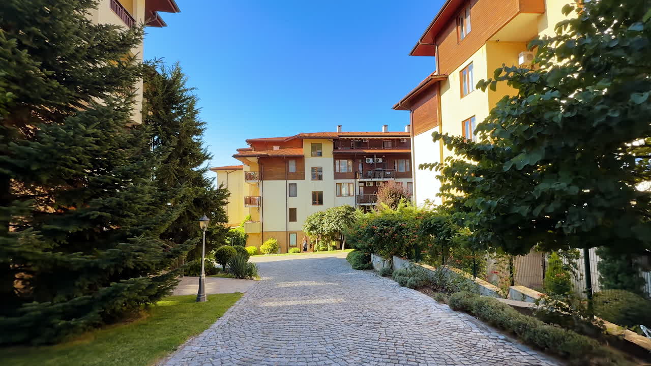 Walk by the paved alley outlined by the green trees. Low angle view on the hotels in Sveti Vlas, Bulgaria