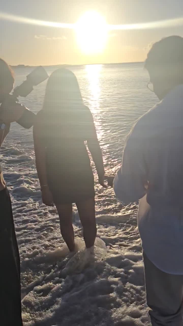 Vertical mobile video capturing a photographer taking romantic engagement photos for a couple along a sunny Caribbean shoreline