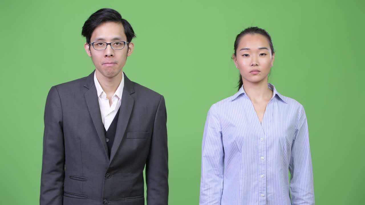 Young Asian business couple pointing at camera together