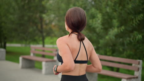 close-up of woman in black fitness wear jogging, with well-kept hair in park, fitness enthusiast enjoying outdoor exercise, healthy lifestyle, running routine, and outdoor workout