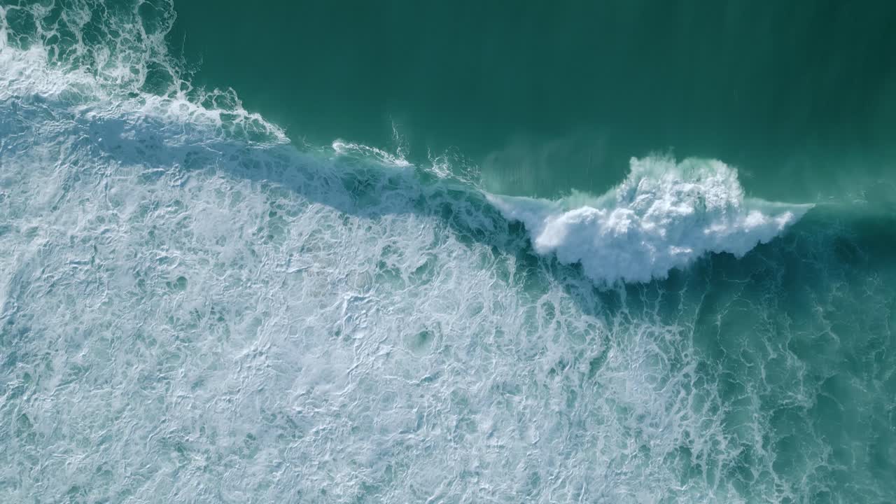 Aerial drone bird's eye view over big waves crashing over sea beach in Nazare, Portugal at daytime