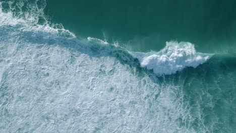 Aerial-drone-bird's-eye-view-over-big-waves-crashing-over-sea-beach-in-Nazare,-Portugal-at-daytime