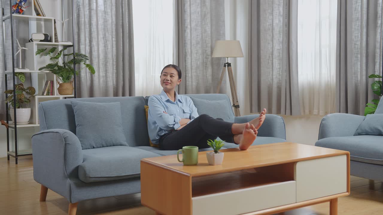 아시아 여자 는 거실 의 소파 에 앉아 있는 나무 테이블 에 발 을 놓는다