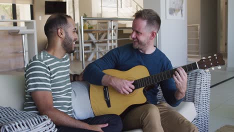 multi ethnic gay male couple sitting on couch one playing guitar