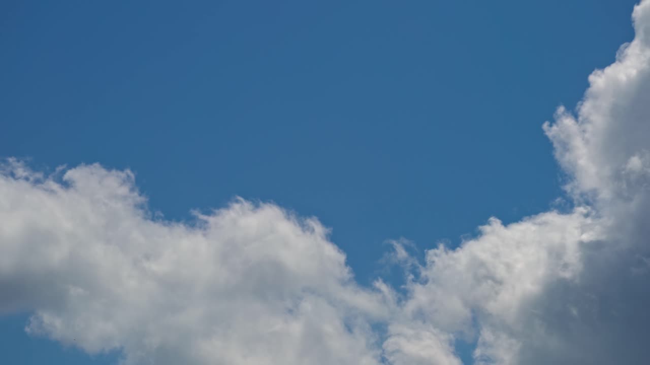 Clouds drift in a blue sky during afternoon hours over an open area