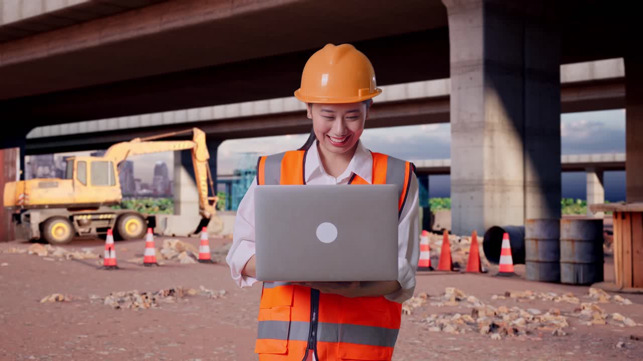 Ingénieure asiatique portant un casque de sécurité et travaillant sur un ordinateur portable tout en se tenant sur le site de construction d’une autoroute