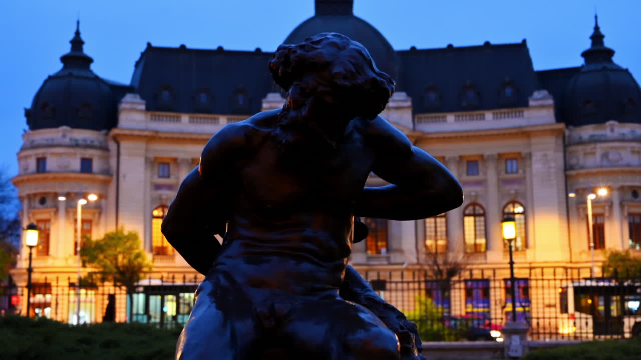 A statue in front of the Central University Library Carol I in Bucharest, Romania in the evening
