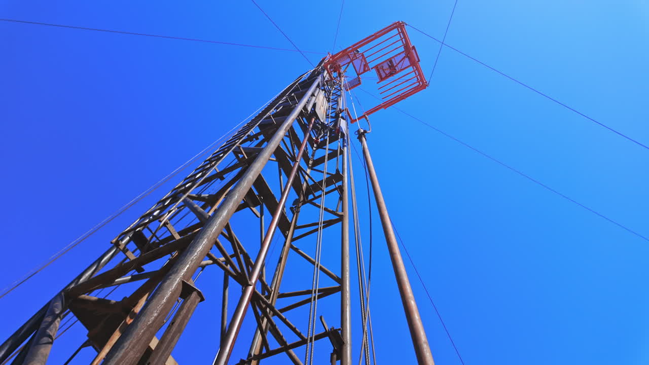 Metal derrick for oil production. Drilling tower at the backdrop of blue clear skies. Low angle view.