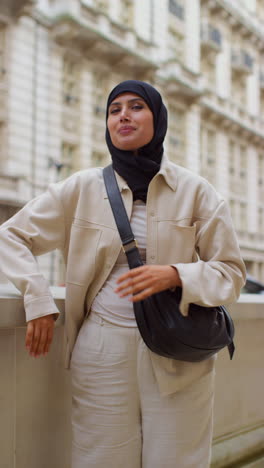 vertical video portrait of smiling muslim businesswoman wearing hijab and modern business suit standing outside city office buildings 2